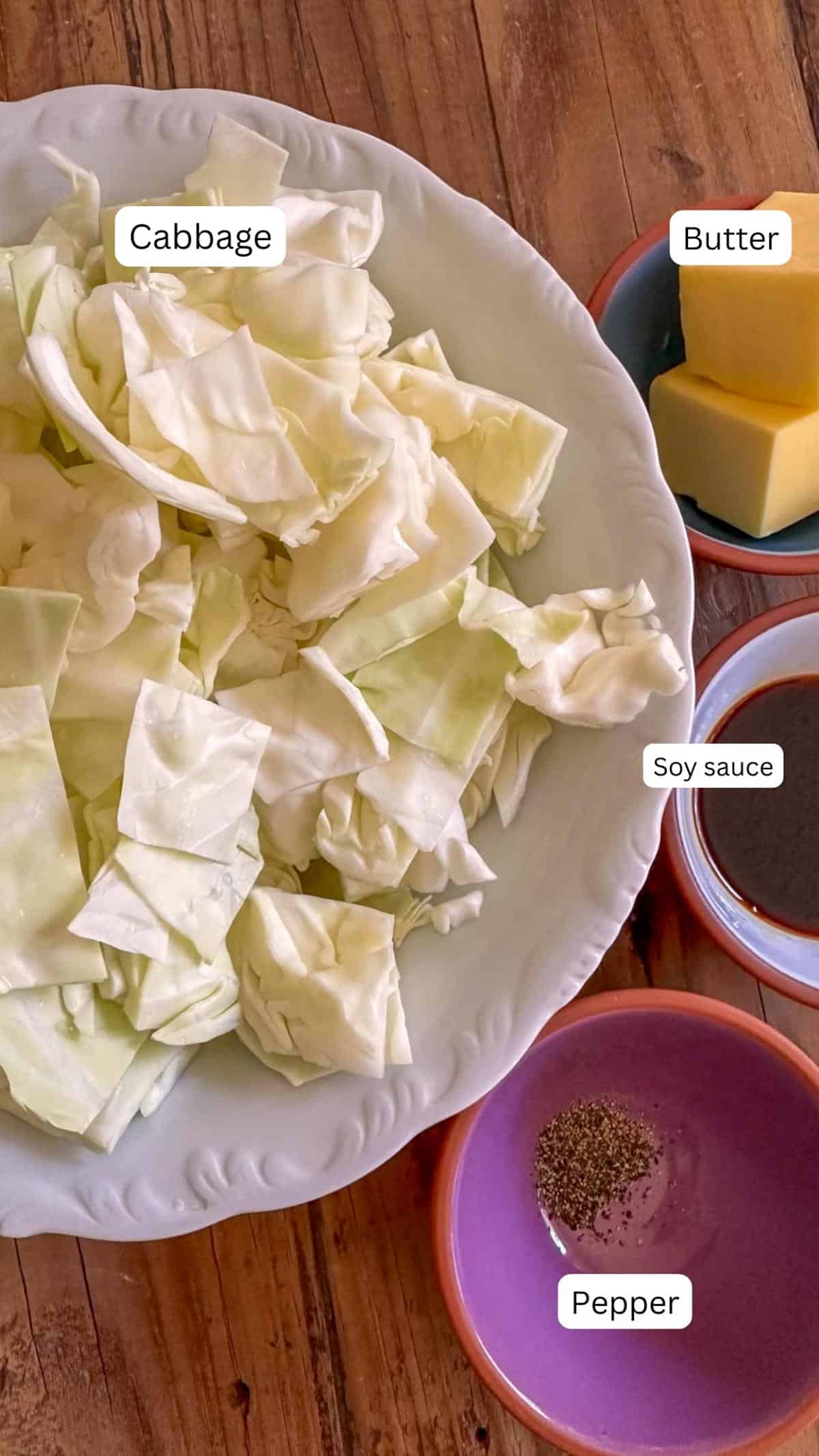 Chopped cabbage in a bowl, and bowls containing pepper, soy sauce, and butter next to the bowl with cabbage.