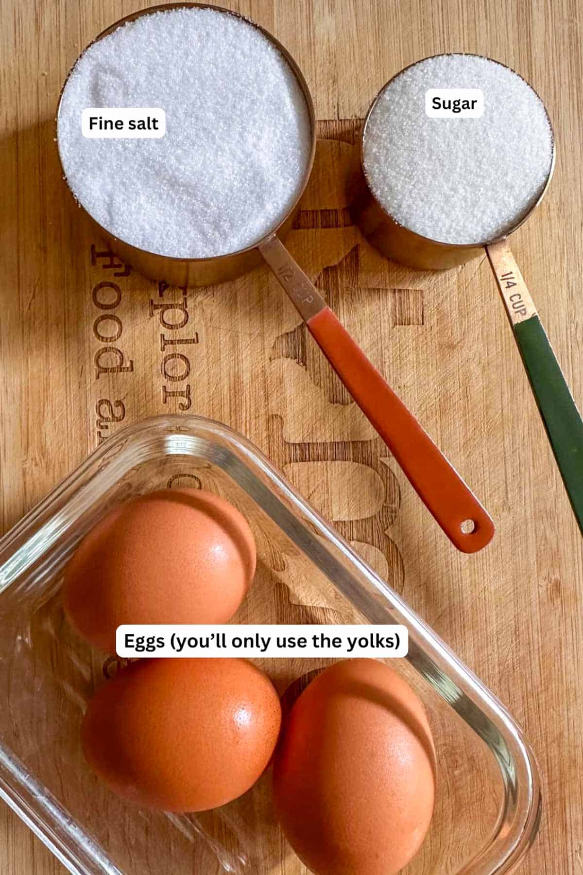 Measuring cups filled with fine salt and sugar, and a glass container with egss.