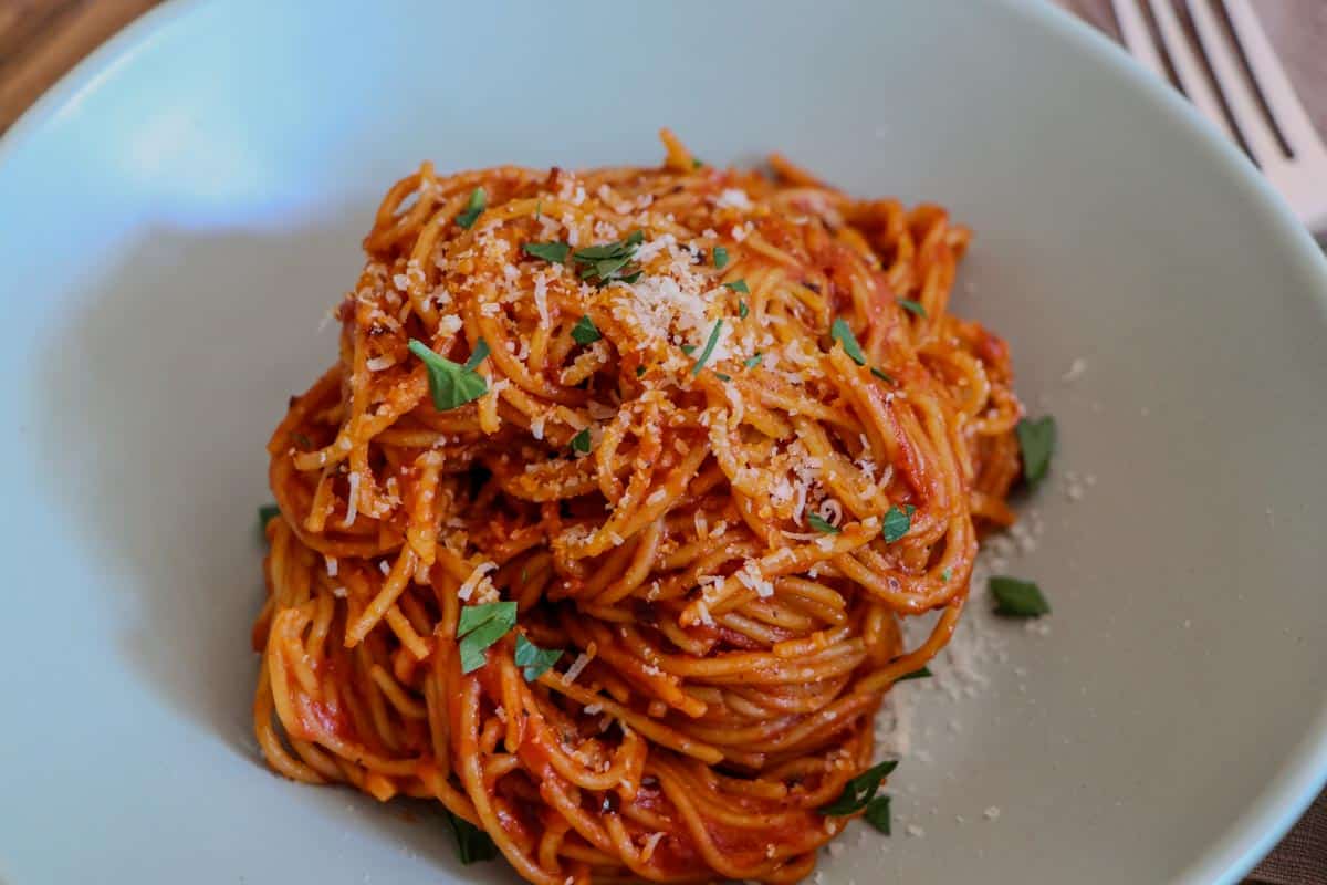 Angel Hair Pasta With Tomato Puree garnished with parsley and Parmesan cheese in a bowl, with a fork on the side.