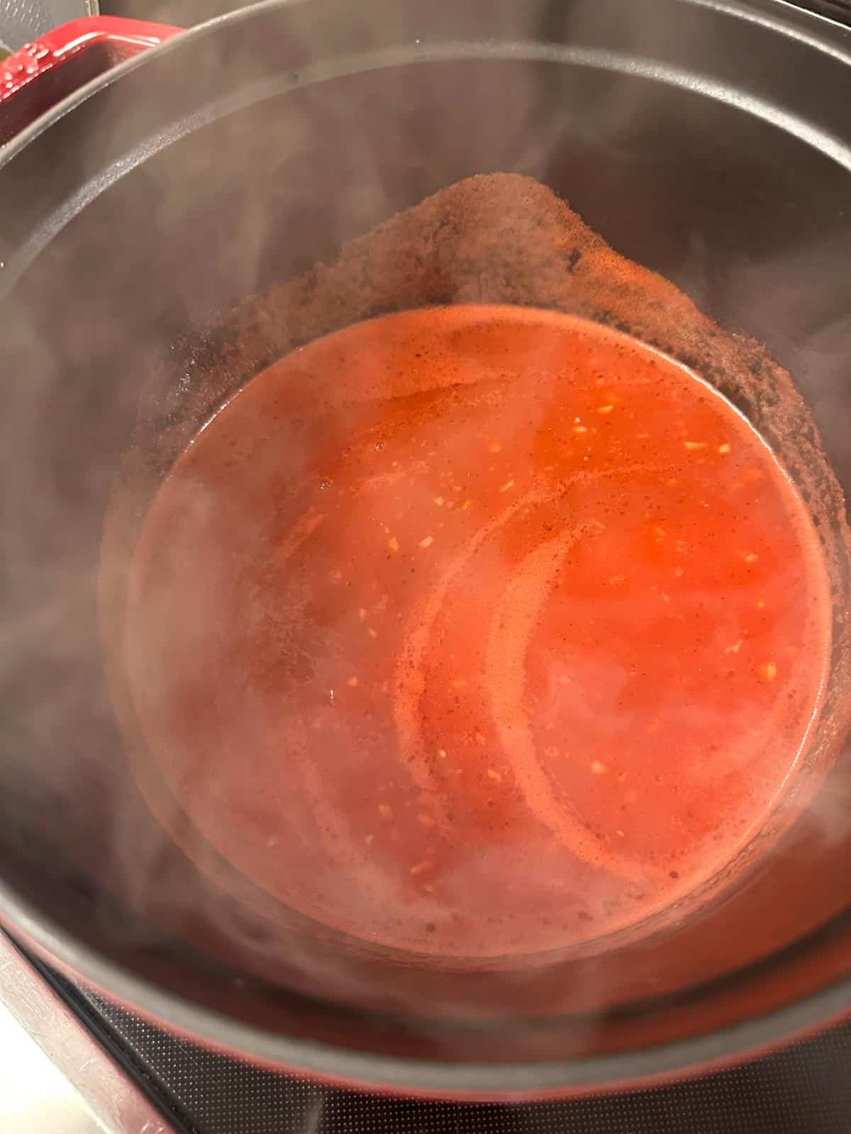 A saucepan containing simmering tomato broth with steam.
