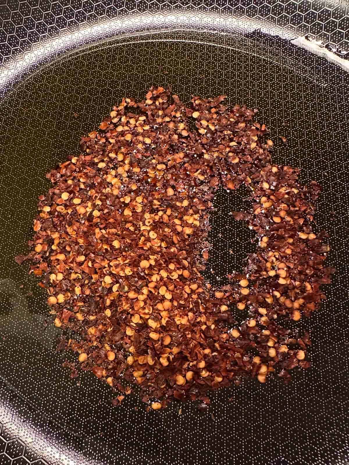 A skillet containing olive oil and red pepper flakes.