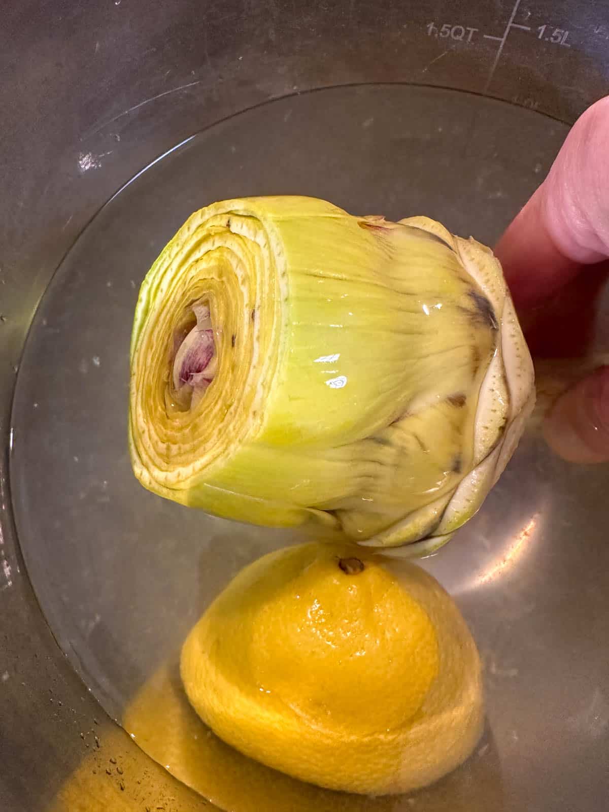 A prepped artichoke and lemon half in a lemon water bath.