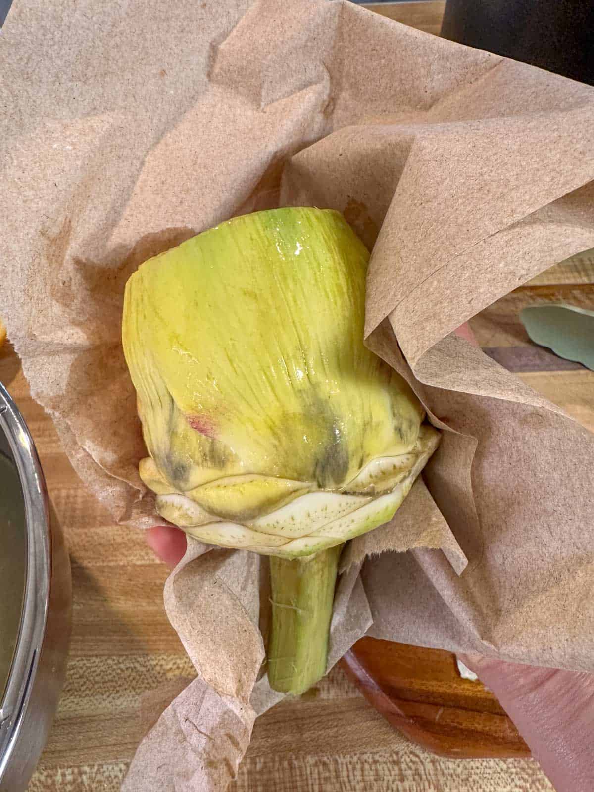 A prepped artichoke being dried in a paper towel.