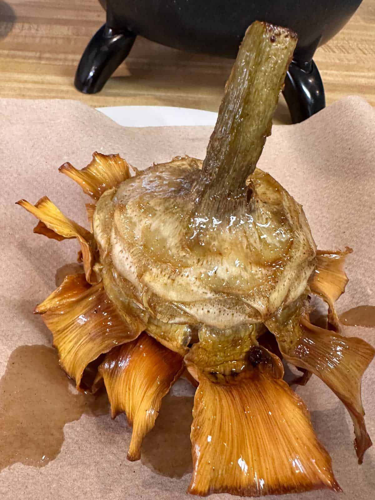 An upside down fried artichoke draining on a paper towel.